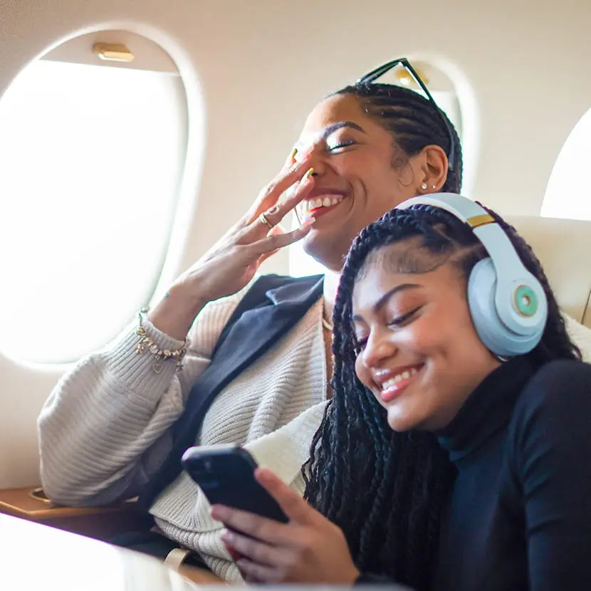 Woman and child sitting next to each other on a plane, sharing a joke and laughing together.