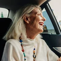 Woman who is travelling as a passenger in the back seat of a car and smiling while looking out of the window.
