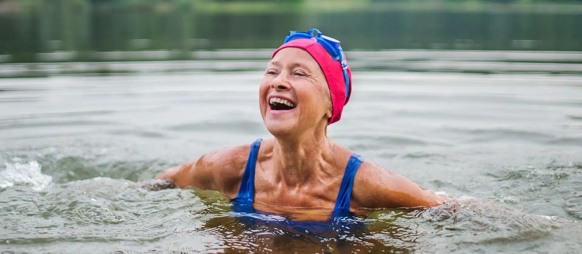 Woman in swimsuit and swimming hat enjoying a cold water swim in a lake on a brisk day.